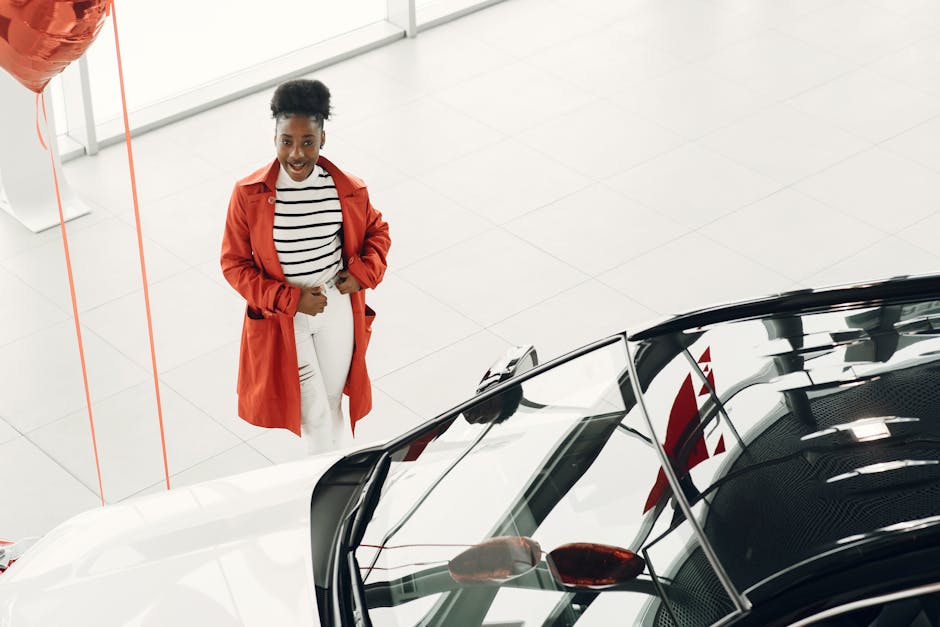 Cheerful woman in red coat exploring a new car at a dealership. Excited car shopping experience